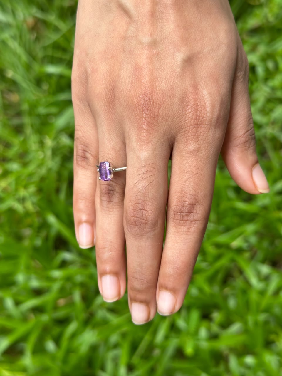 1.45 ct Natural Heat-Treated Purple Sapphire set in a ring worn on a hand, showcasing its elegant design against a green background.