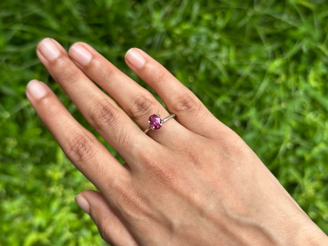 1.65 ct unheated Oval Ruby ring showcased on a hand against a lush green background, highlighting its vibrant color and setting.