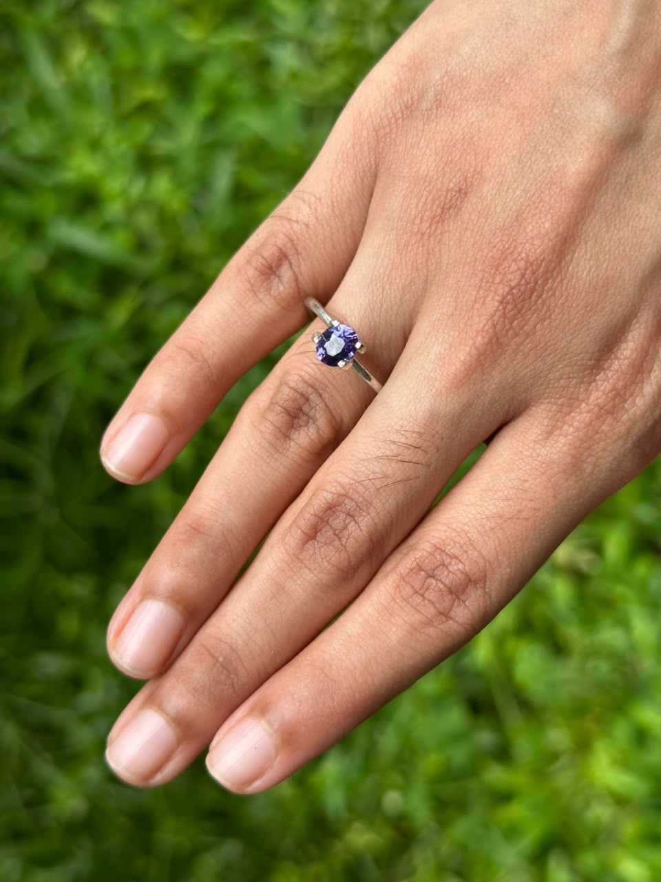 1.20 ct Oval Purple Sapphire set in a ring, showcased on a hand against a grassy background.