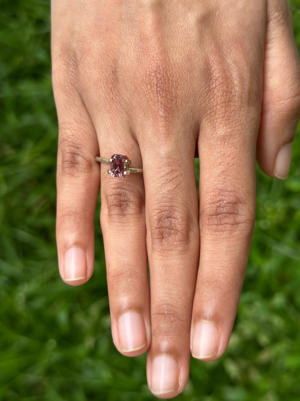 1.62 ct Emerald-Cut Brown Sapphire ring displayed on a hand in a grassy setting.