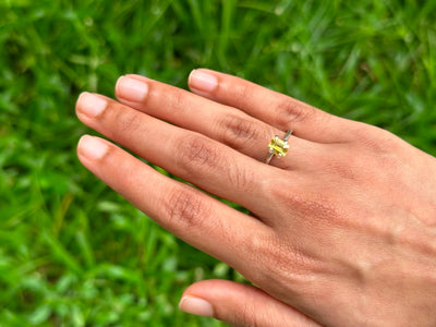 Hand wearing a ring featuring a 1.17 ct Emerald-Cut Ceylon Yellow Sapphire on green grass background.