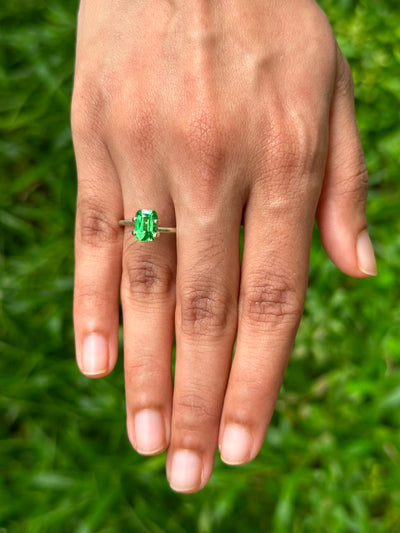 1.86 ct Cushion Tsavorite garnet ring displayed on a hand, surrounded by green grass.