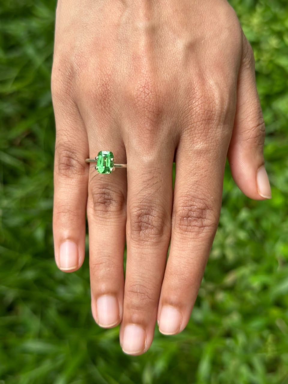1.86 ct Cushion Tsavorite garnet ring displayed on a hand, surrounded by green grass.