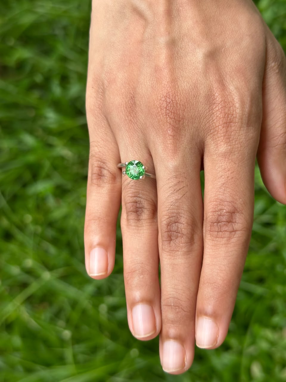 1.79 ct Round Tsavorite Garnet ring displayed on a hand, set against a green grass background.