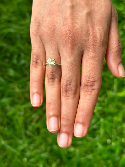 Hand wearing a 1.44 ct Round Ceylon Yellow Sapphire engagement ring on green grass.